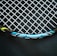 A close-up view of a tennis racket featuring a mesh pattern of white strings against a dark background. The rim of the racket is visible with blue, black, and yellow accents, and the text 'ENGINEERED POWER' is prominently displayed on the frame.